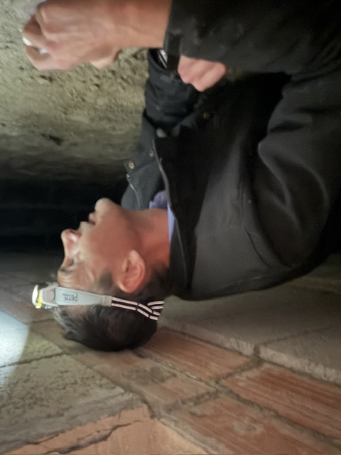 Sylvain Trioux, lampe frontale allumée, inspectant un espace de très faible hauteur sous un plancher